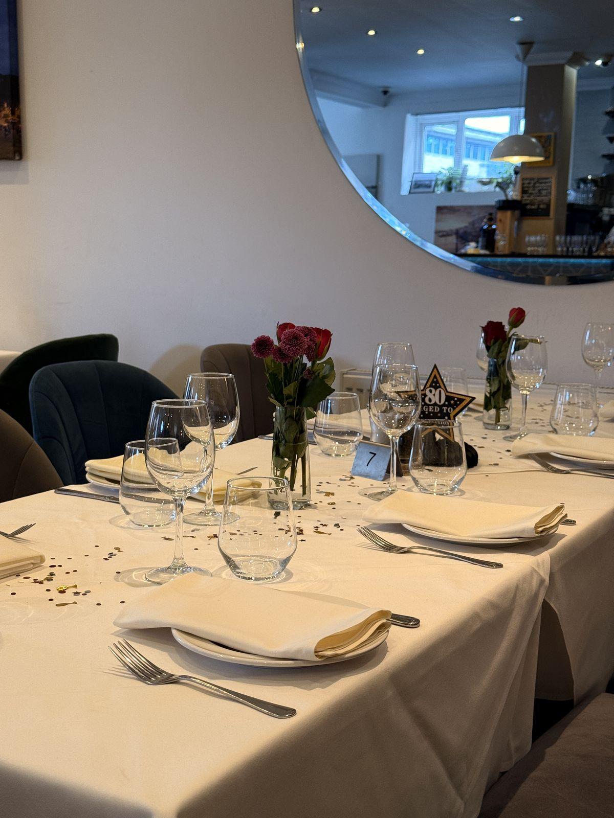 Tables dressed in white linen with roses and 80th birthday place cards