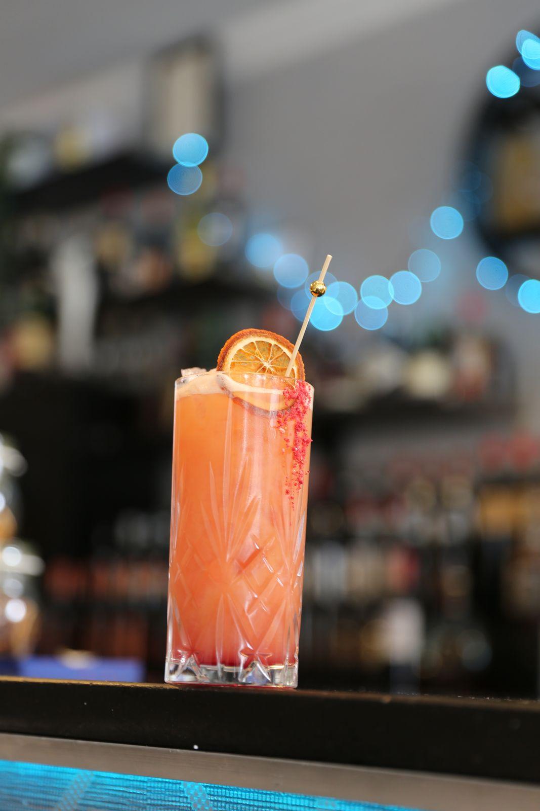 A pink spritz with a sugared rim under bar lights