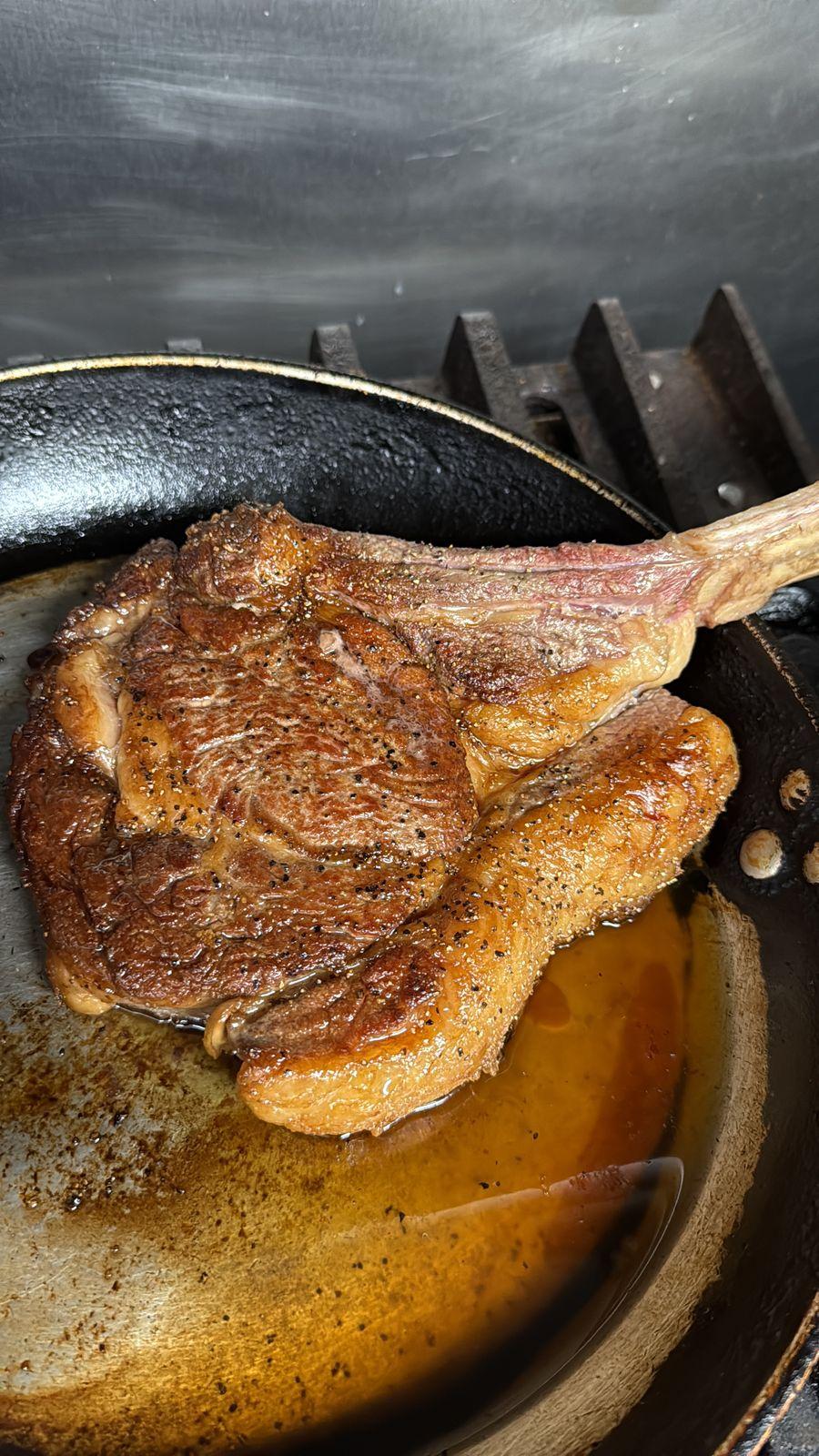 A bone-in tomahawk steak searing in the pan