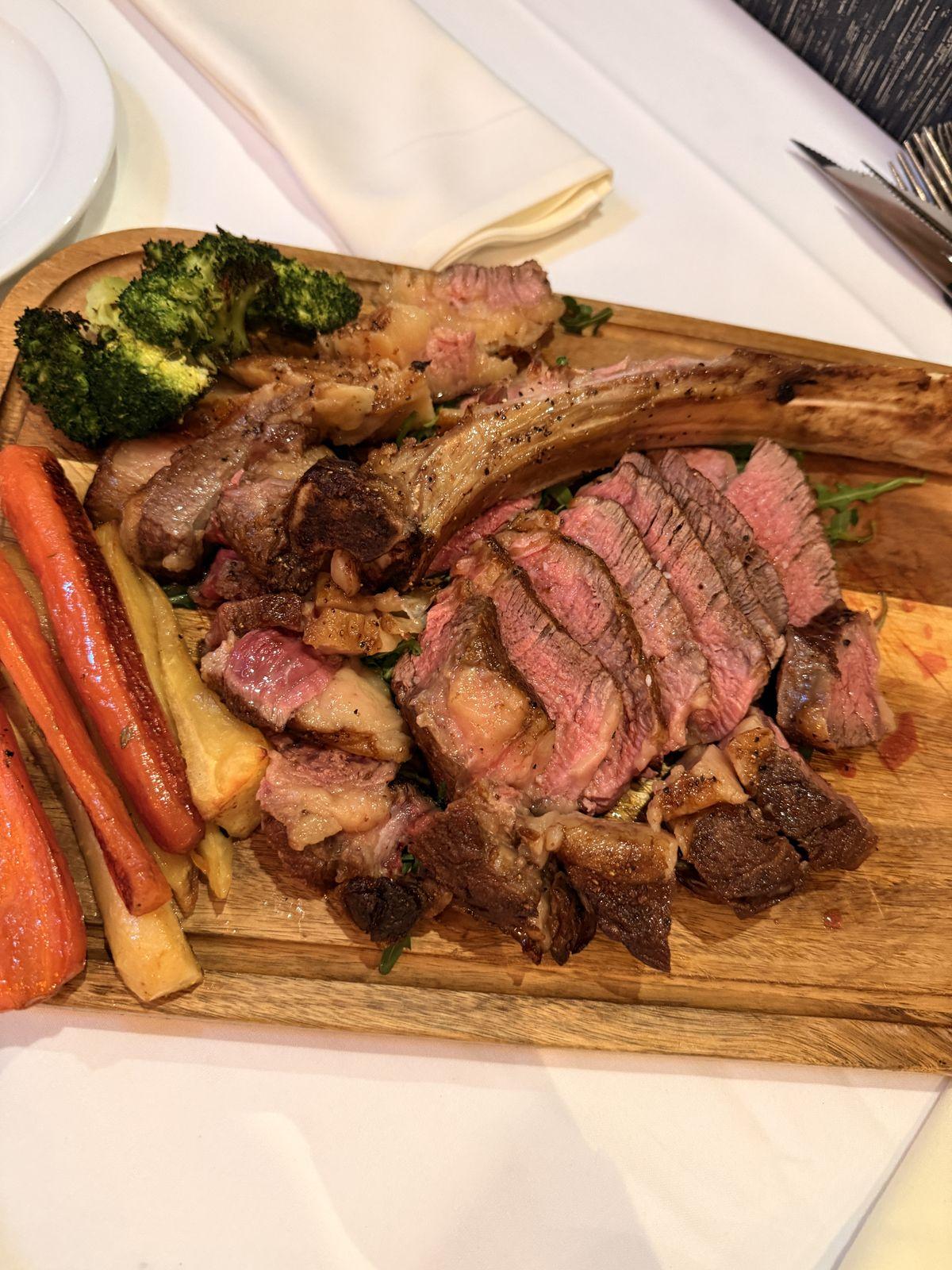 Sliced tomahawk steak served on a board with vegetables